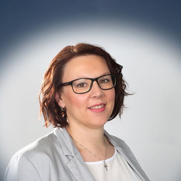 Das Bild zeigt eine Frau mit grauen Blazer und einer Brille