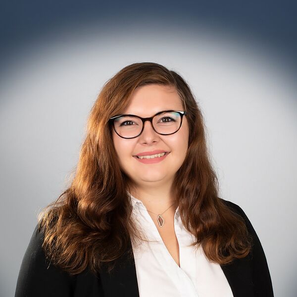 Das Bild zeigt eine Frau mit Anzug und Brille